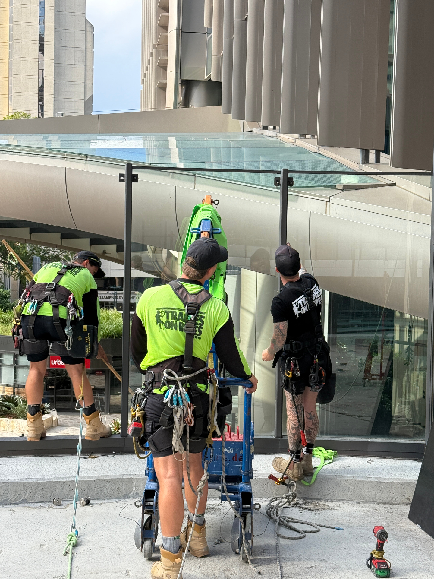 Three Tradies on Ropes technicians installing curved glass canopy panels at 1 William Street Brisbane