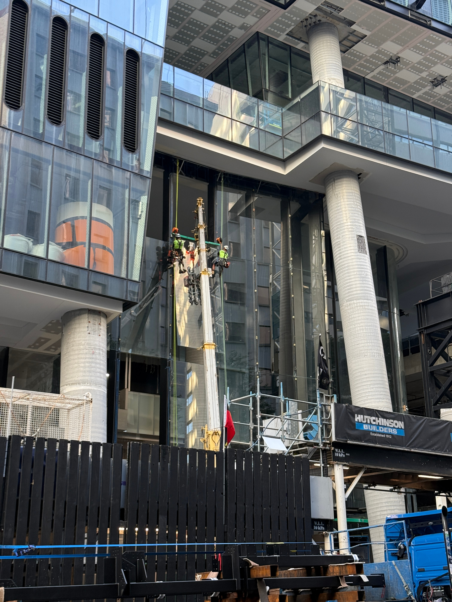Rope access glaziers installing curtain wall glass behind Hutchinson Builders hoarding at 360 Queen Street