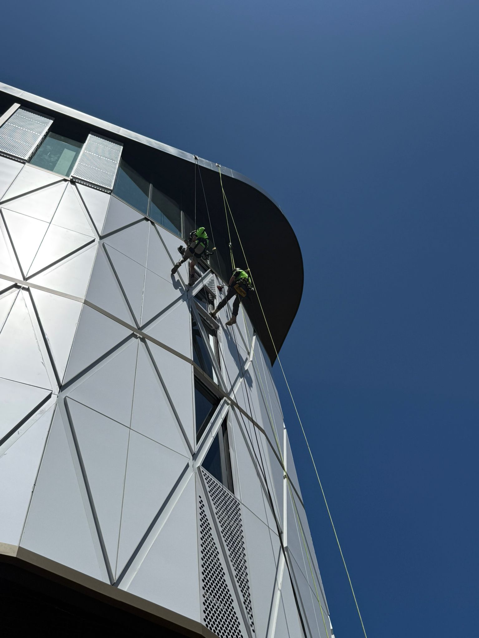Two rope access technicians working on the upper façade of Ascent on Bourke in Alexandria