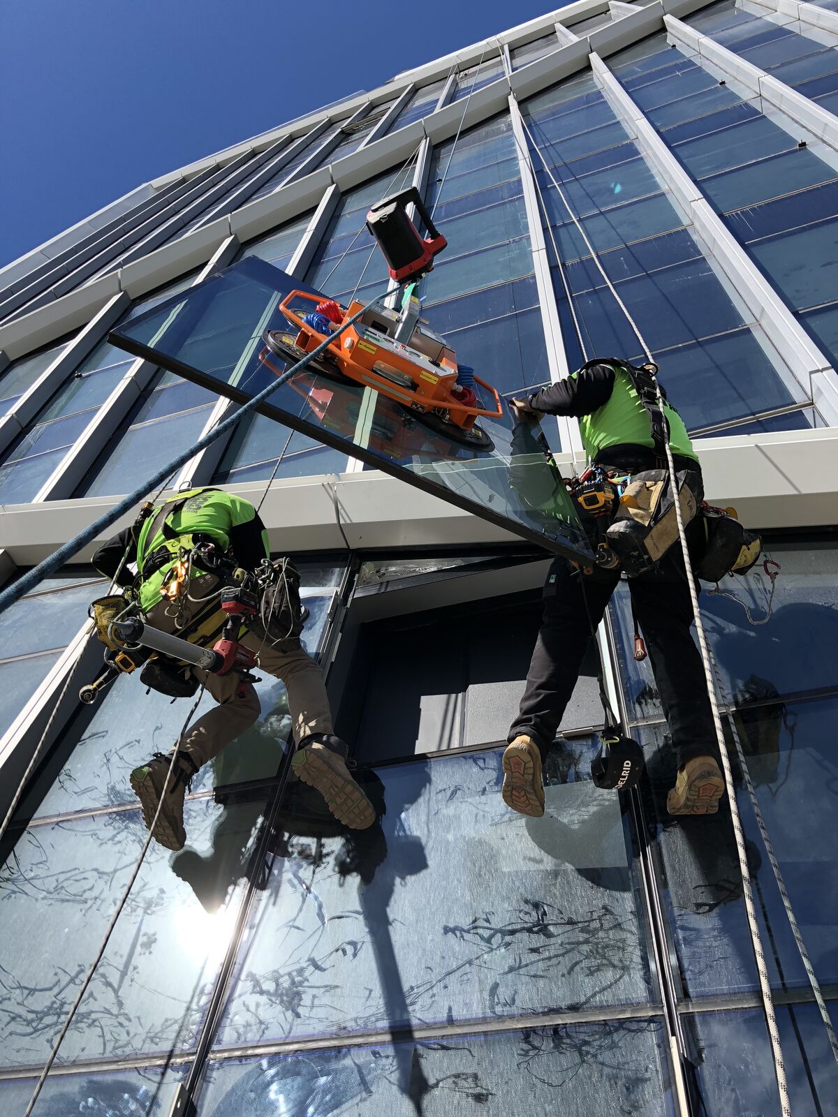 Rope access glass panel installation using suction lifter on Jewel façade