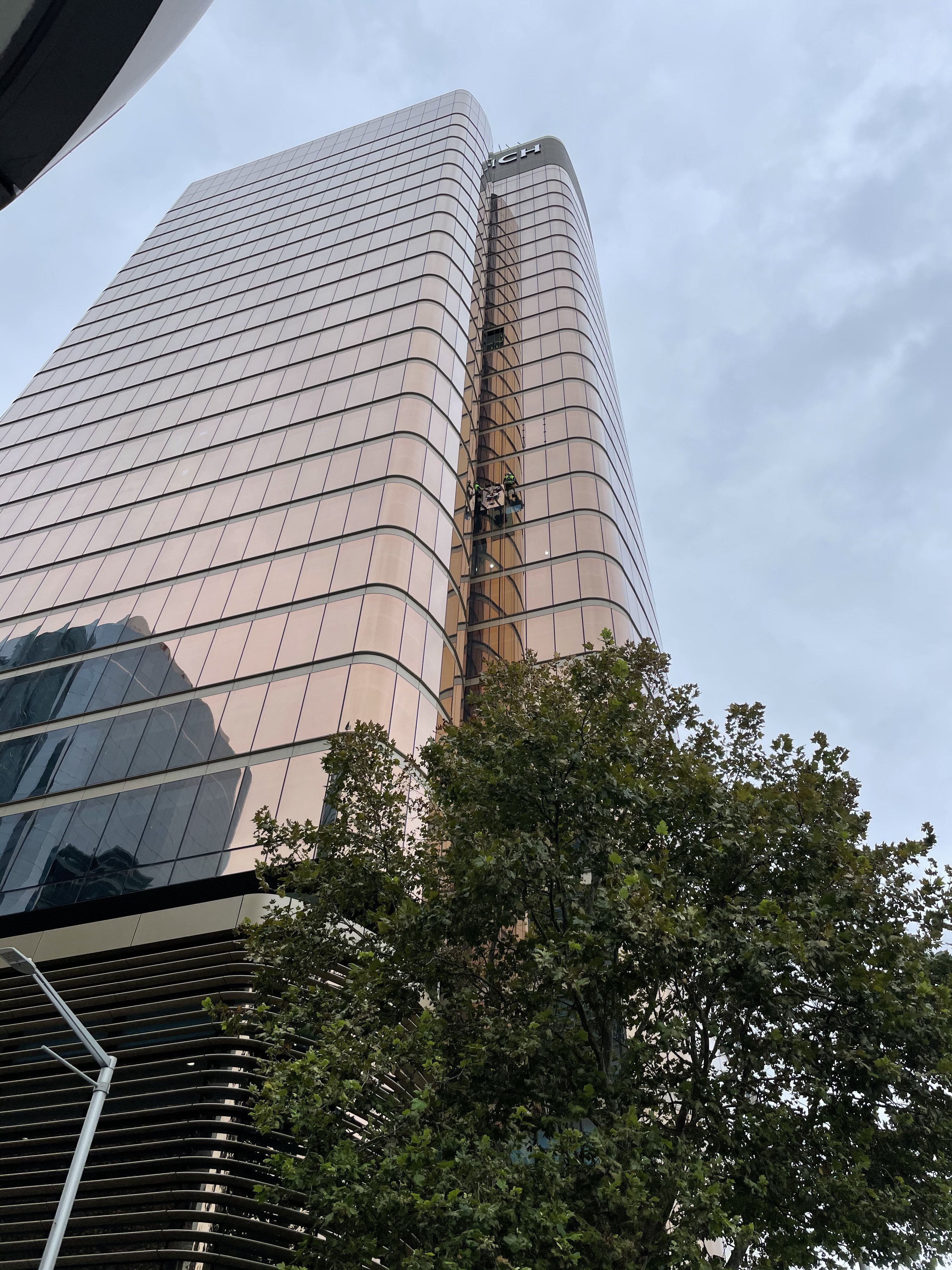 Wide street-level view of Zurich Tower in North Sydney with rope access crew working on the corner façade